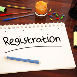 Photo of a pens and a spiral notepad on a tabletop, with the word Registration hand written on the pad.